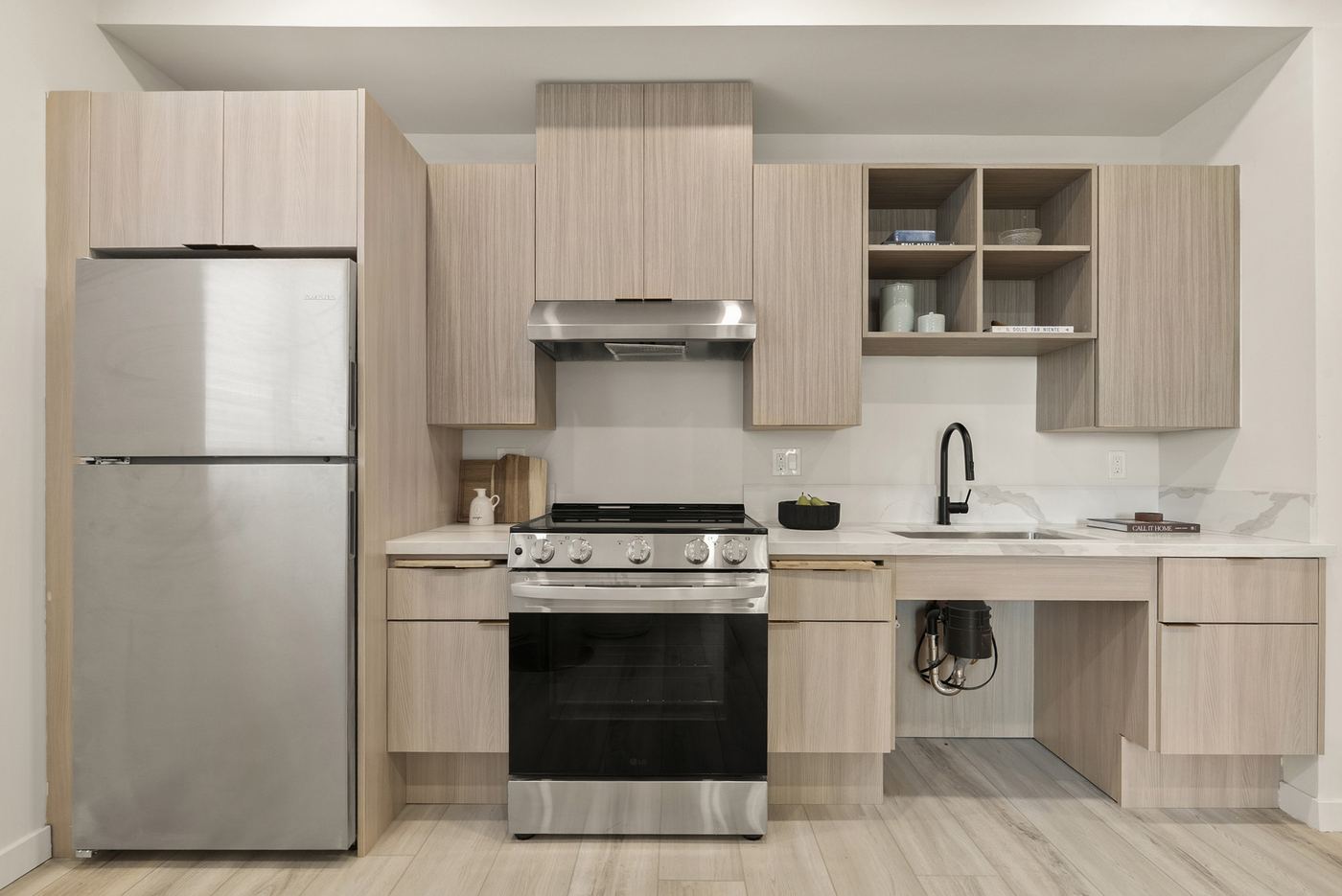 An apartment kitchen with a gas range, a refrigerator, wood-tone cabinets, and a sink with open space underneath.