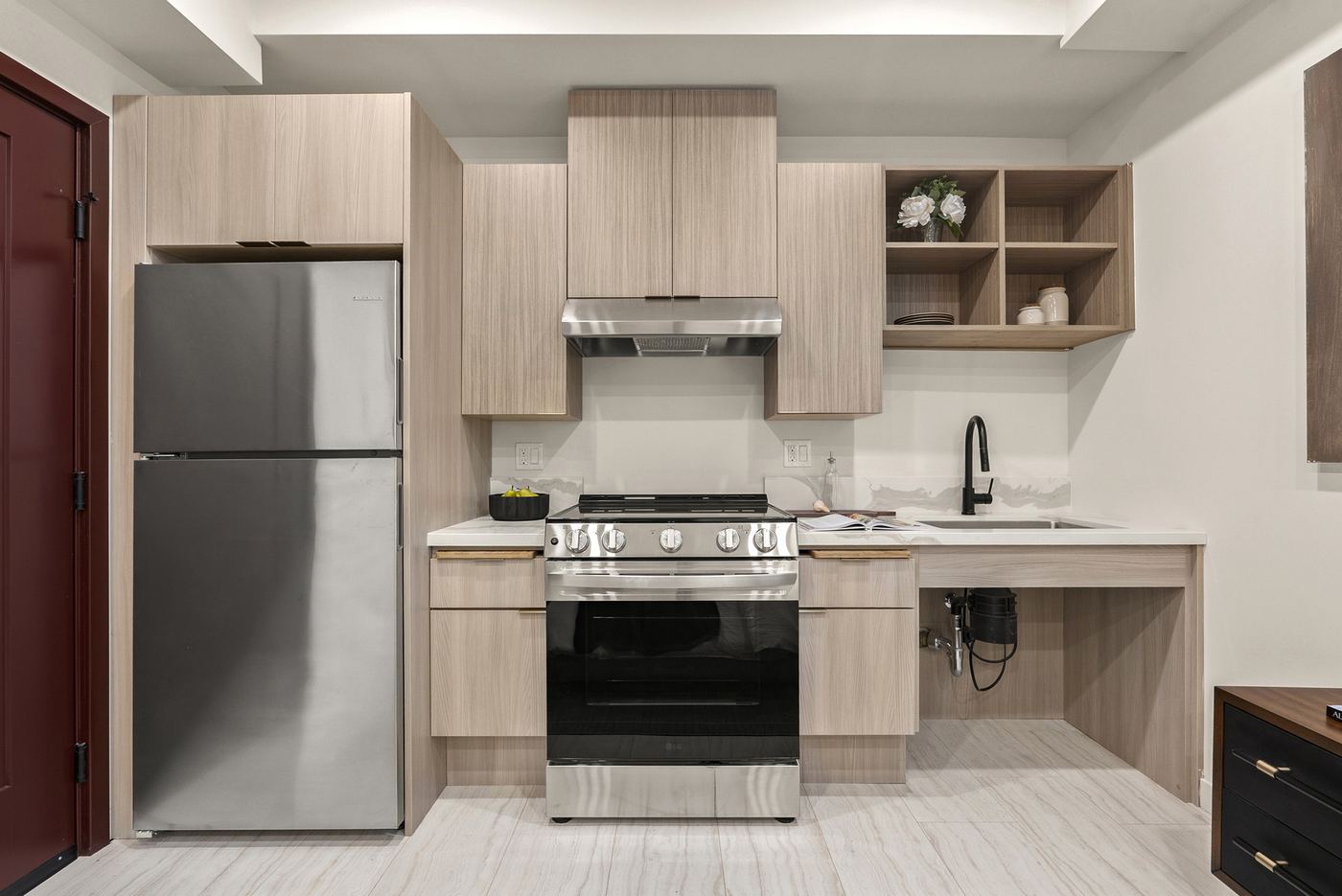 A kitchen with an electric range, a refrigerator, counters on two walls, and a sink with open space underneath.